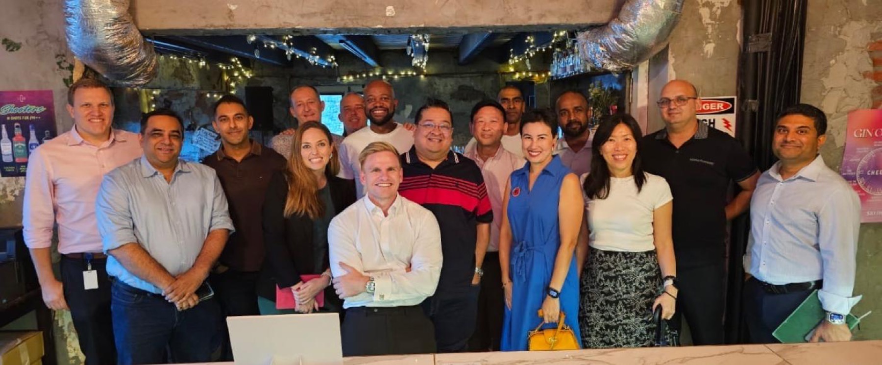 Fifteen members standing together for a group photograph at a bar