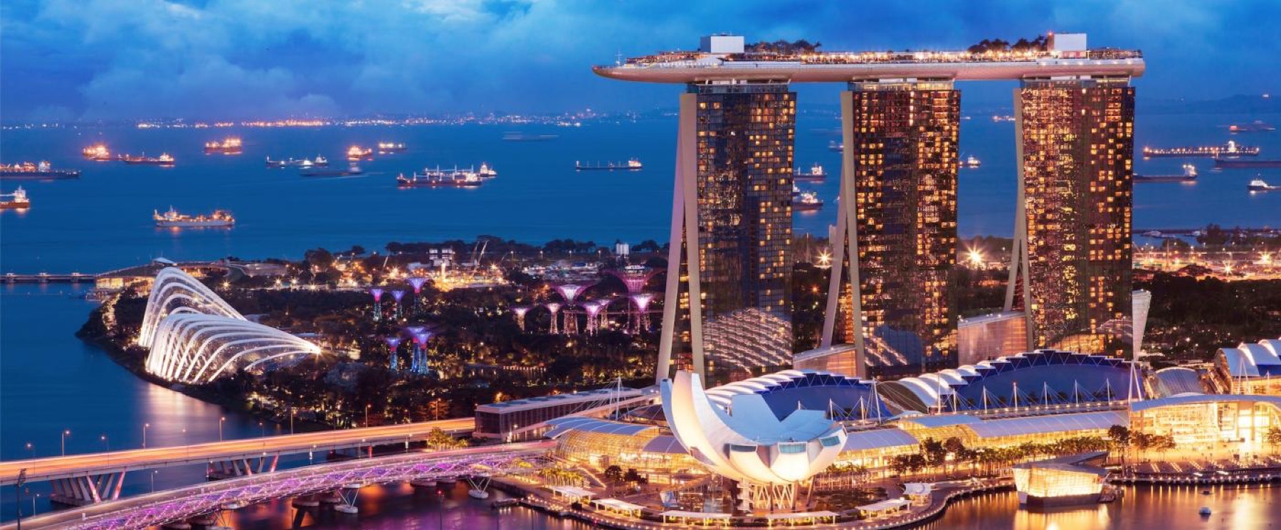 Marina Bay, Singapore, at dusk, with the bay full of anchored shipping behind it